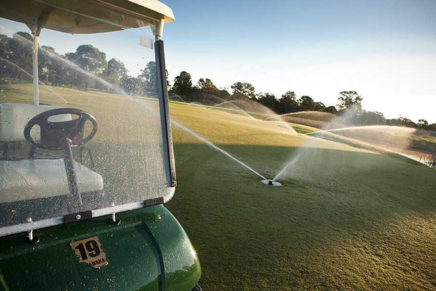 Golf cart in front of sprinklers on golf course